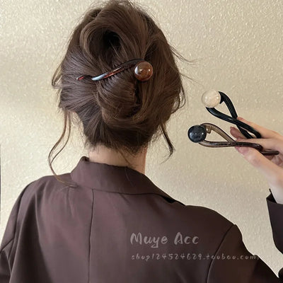 Elegant hairpin securing a twisted updo, featuring a brown marbled sphere on a curved plastic clip.